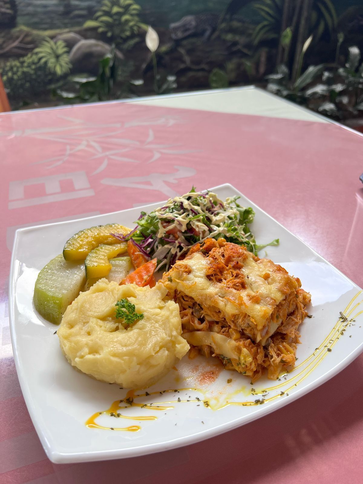 Une assiette de nourriture comprenant une salade, de la purée de pommes de terre et un plat en couches, qui pourrait être des lasagnes, le tout servi dans une assiette blanche.