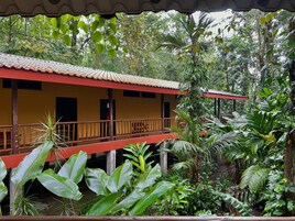 Um edifício de dois andares com telhado vermelho e paredes amarelas, rodeado por vegetação tropical exuberante.