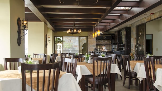 Een restaurant met houten tafels en stoelen, een keuken op de achtergrond en een kroonluchter.