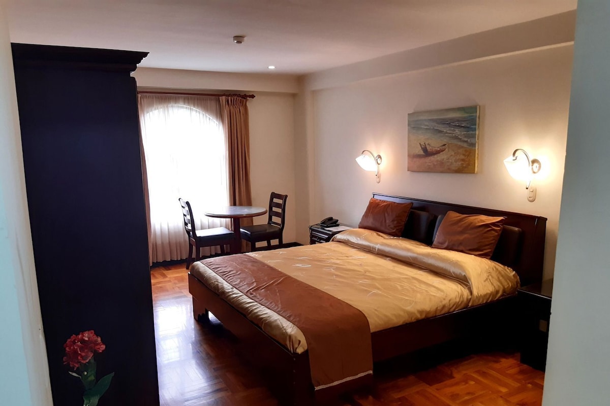 Une chambre à coucher avec un lit, des tables de chevet, un bureau avec des chaises et un tableau au mur.
