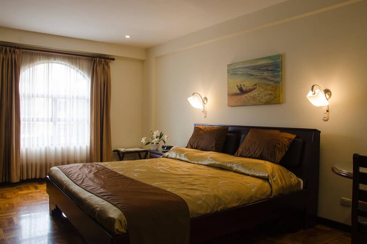 Ein Hotelzimmer mit Bett, Nachttisch, einem Gemälde und einem Fenster mit Vorhängen.