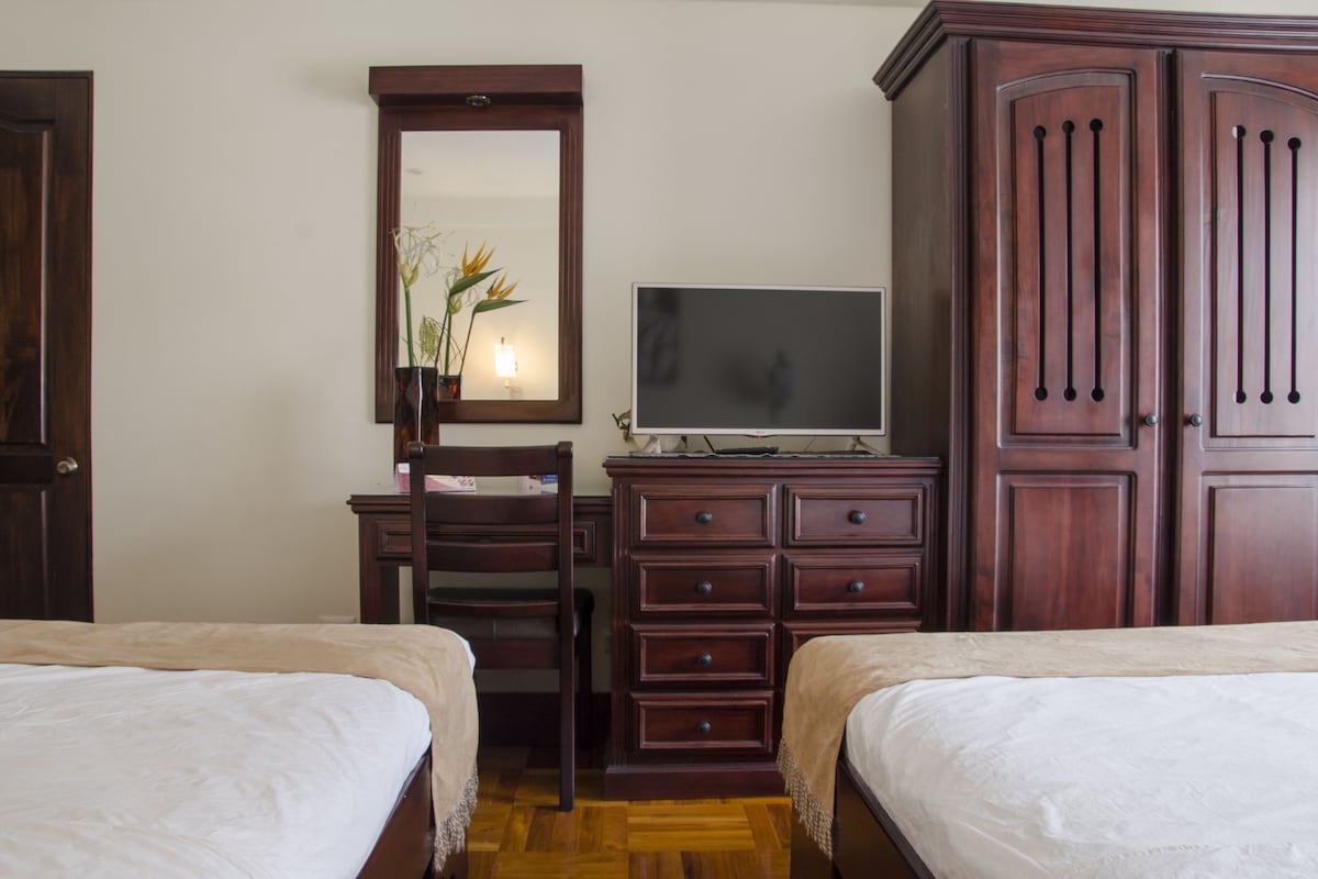 Une chambre avec deux lits, une commode, un téléviseur et un miroir.