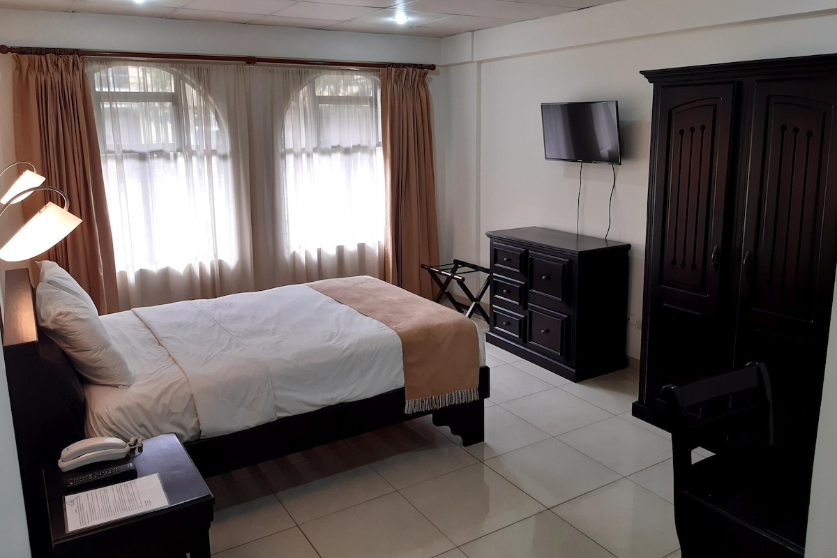 Une chambre d’hôtel comprenant un lit, un bureau avec une lampe, un téléphone, un téléviseur posé sur un meuble et une armoire.