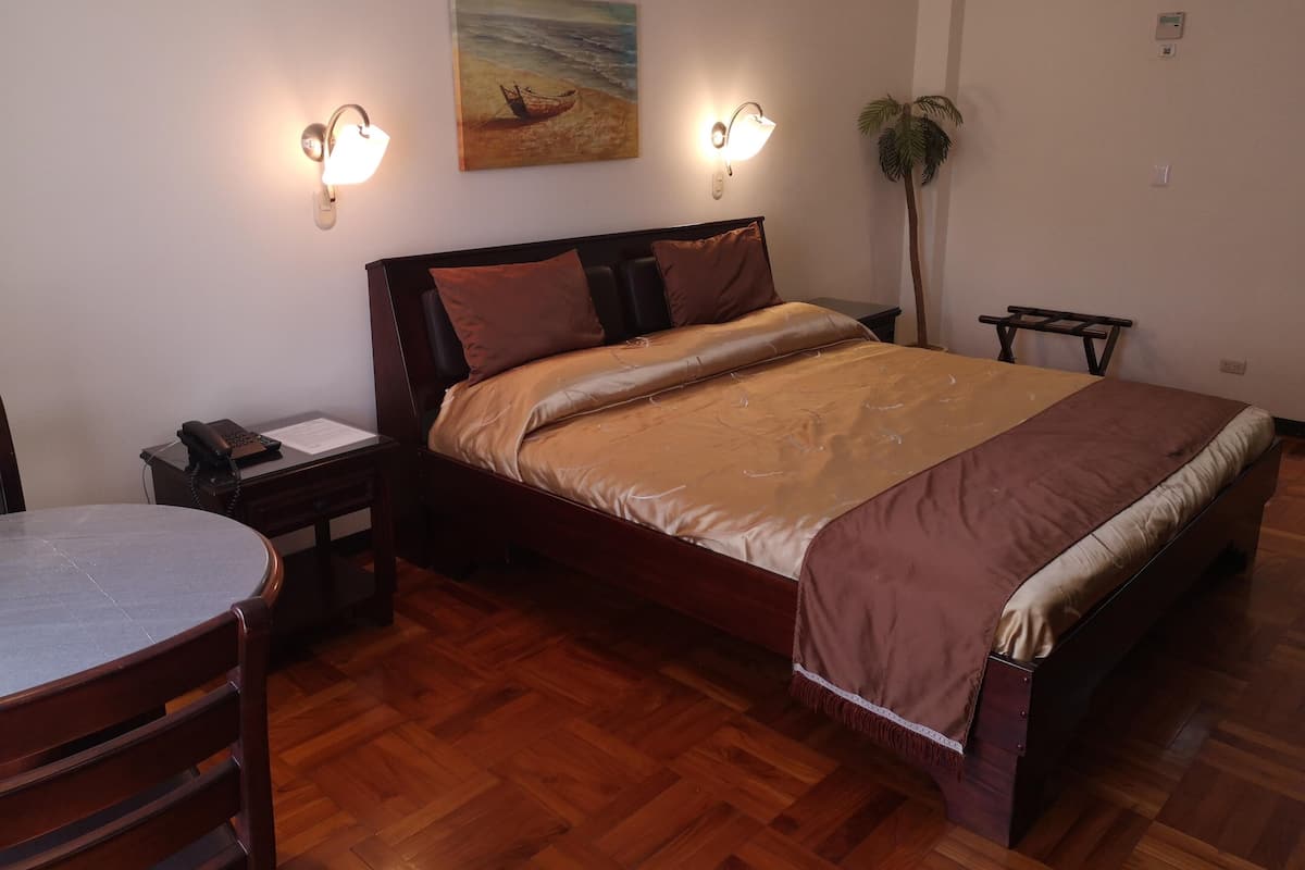 Ein ordentlich eingerichtetes Schlafzimmer mit einem hölzernen Bett, einem Nachttisch mit Lampe, einem Sessel und einem Bild an der Wand.