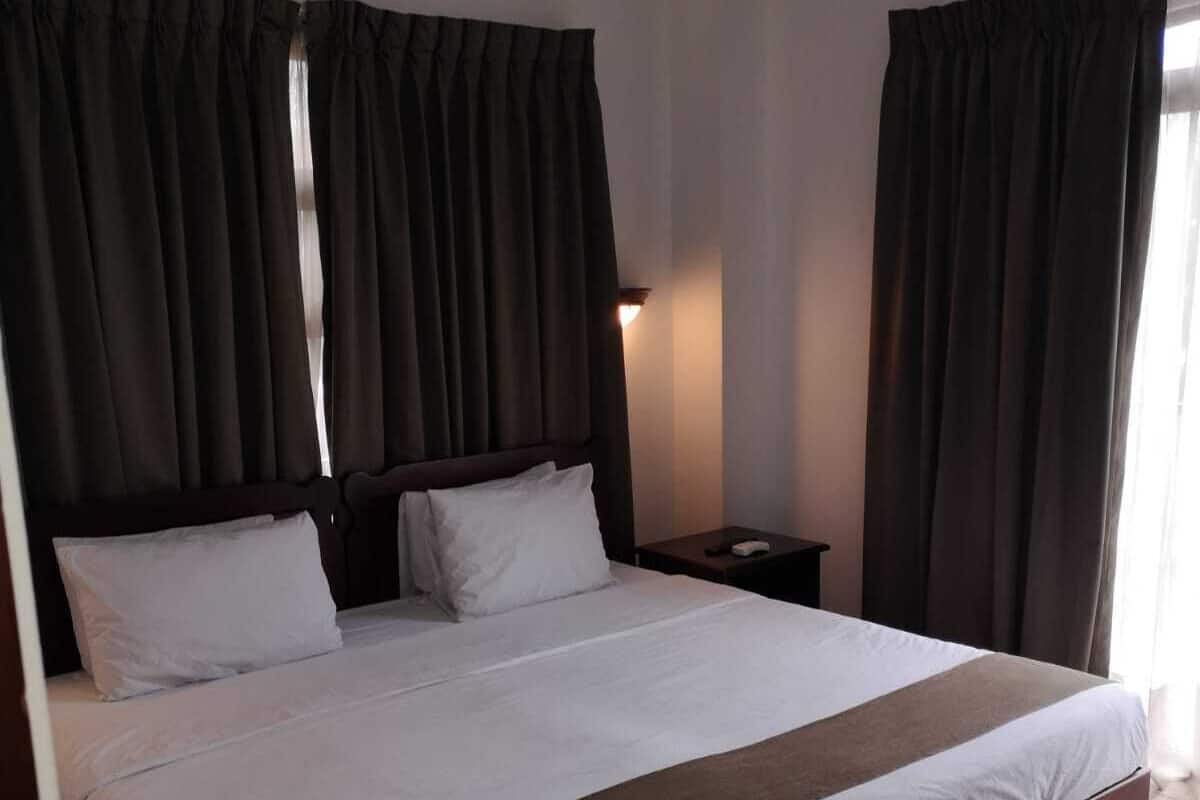 Ein modernes Hotelzimmer mit einem großen Bett, dunklen Vorhängen, einem Nachttisch und einem Beistelltisch.