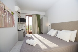 A hotel room with a bed, a desk, a TV, and a balcony with curtains. - John & Mary's Studios (Rhodes)