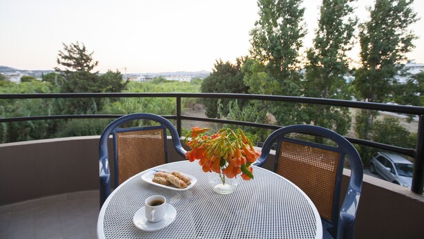 Ein Balkon mit Tisch, Stühlen, einer Blumenvase, einem Tablett mit Gebäck und einer Kaffeetasse.