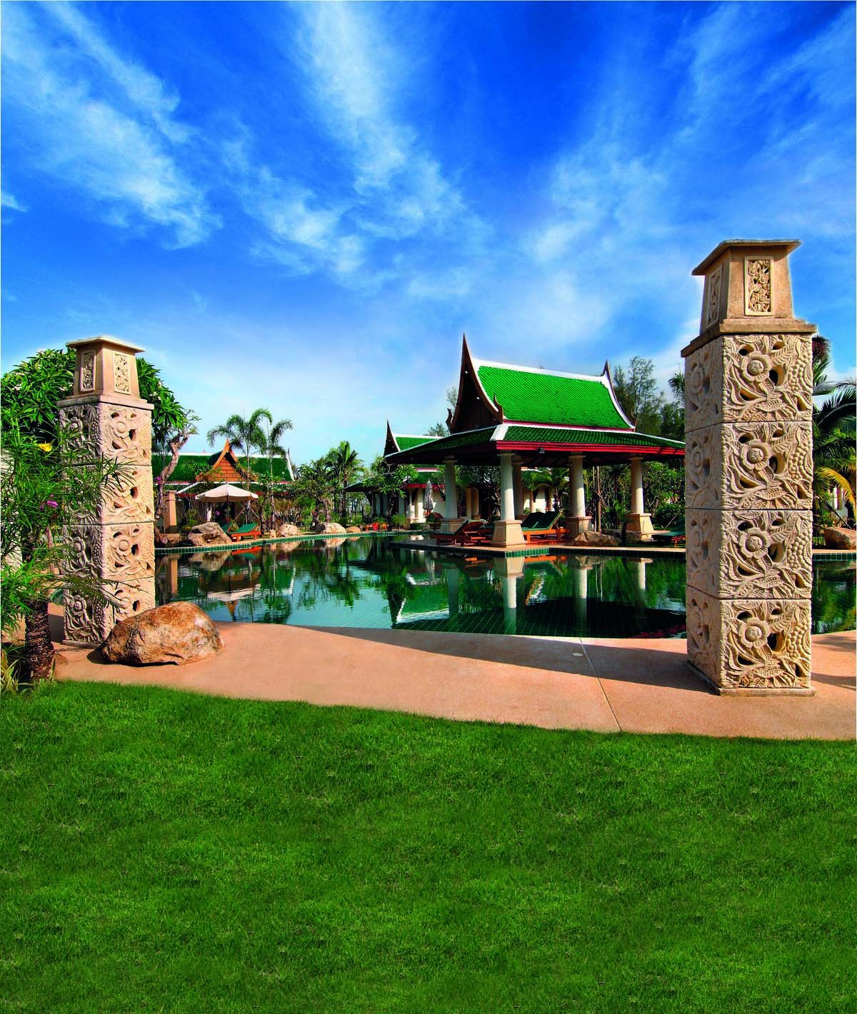 A traditional-style building with a green roof, surrounded by a pool and palm trees.