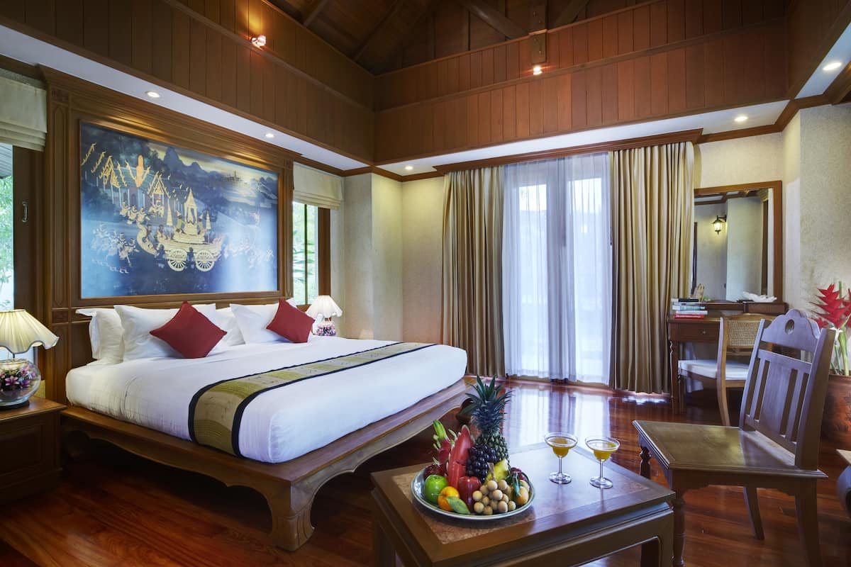 A hotel room with a large bed, wooden furniture, a fruit and drink tray, and a painting on the wall.
