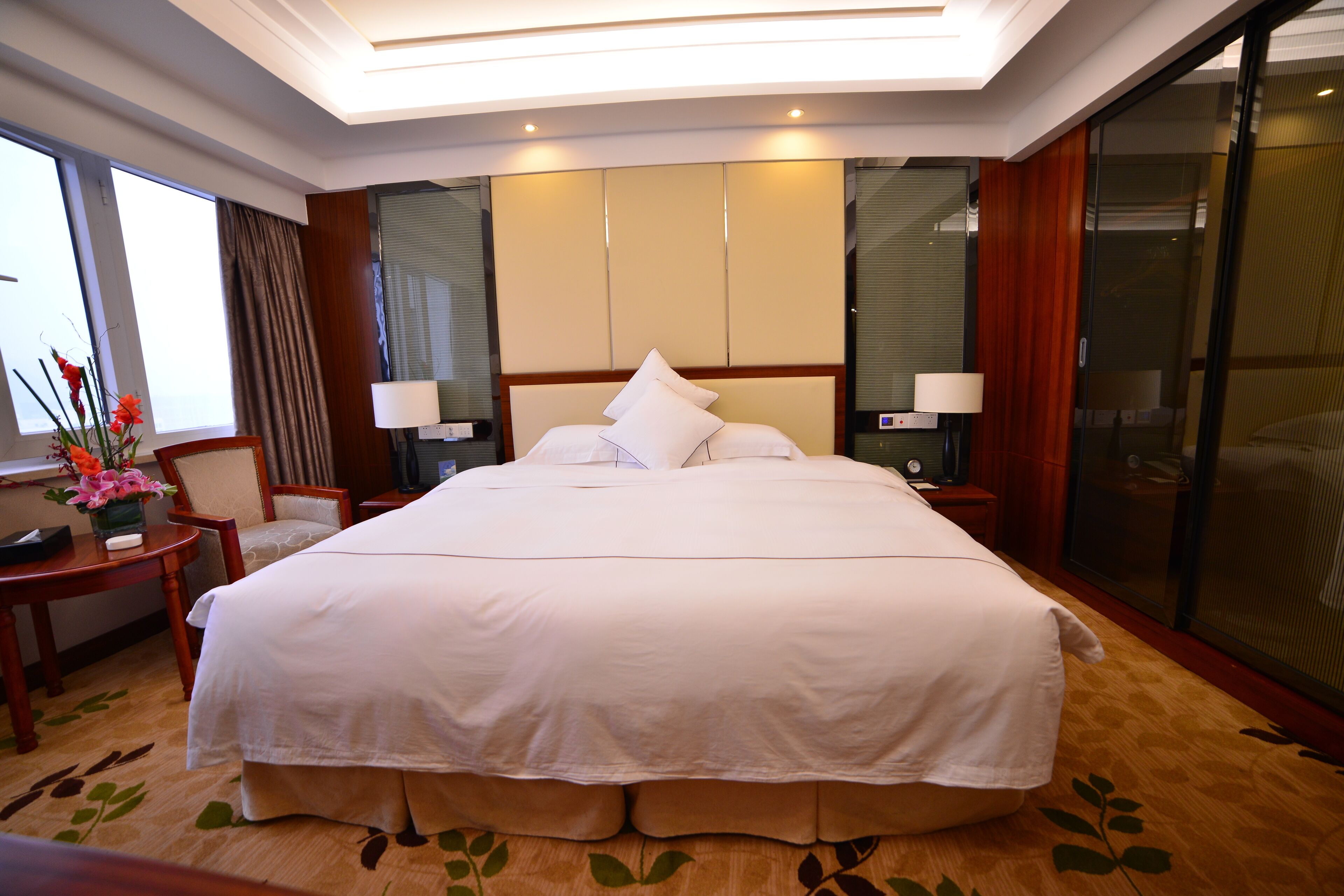 A large bed with white linens, a bedside table with a lamp, and a chair.
