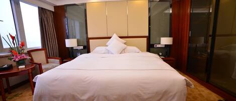 A large bed with white linens, a bedside table with a lamp, and a chair.