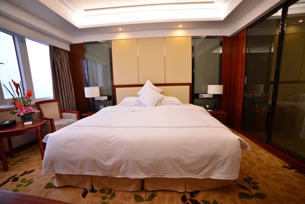A large bed with white linens, a bedside table with a lamp, and a chair. - Guizhou Park Hotel (Guiyang)