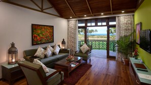 A living room with a wooden ceiling, a green sofa with floral cushions, a coffee table, and a view of the ocean through large windows. - Caravela Beach Resort (Varca)