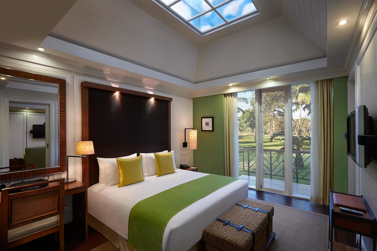 A hotel room with a large bed, a desk, a chair, a TV, and a balcony with a view of the outdoors.