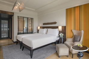 A hotel room with a large bed, a chair, a small table, and a decorative wall panel.