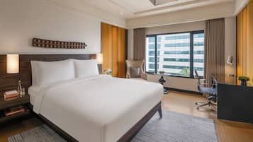 A modern hotel room with a large bed, a desk, and a view of a cityscape.