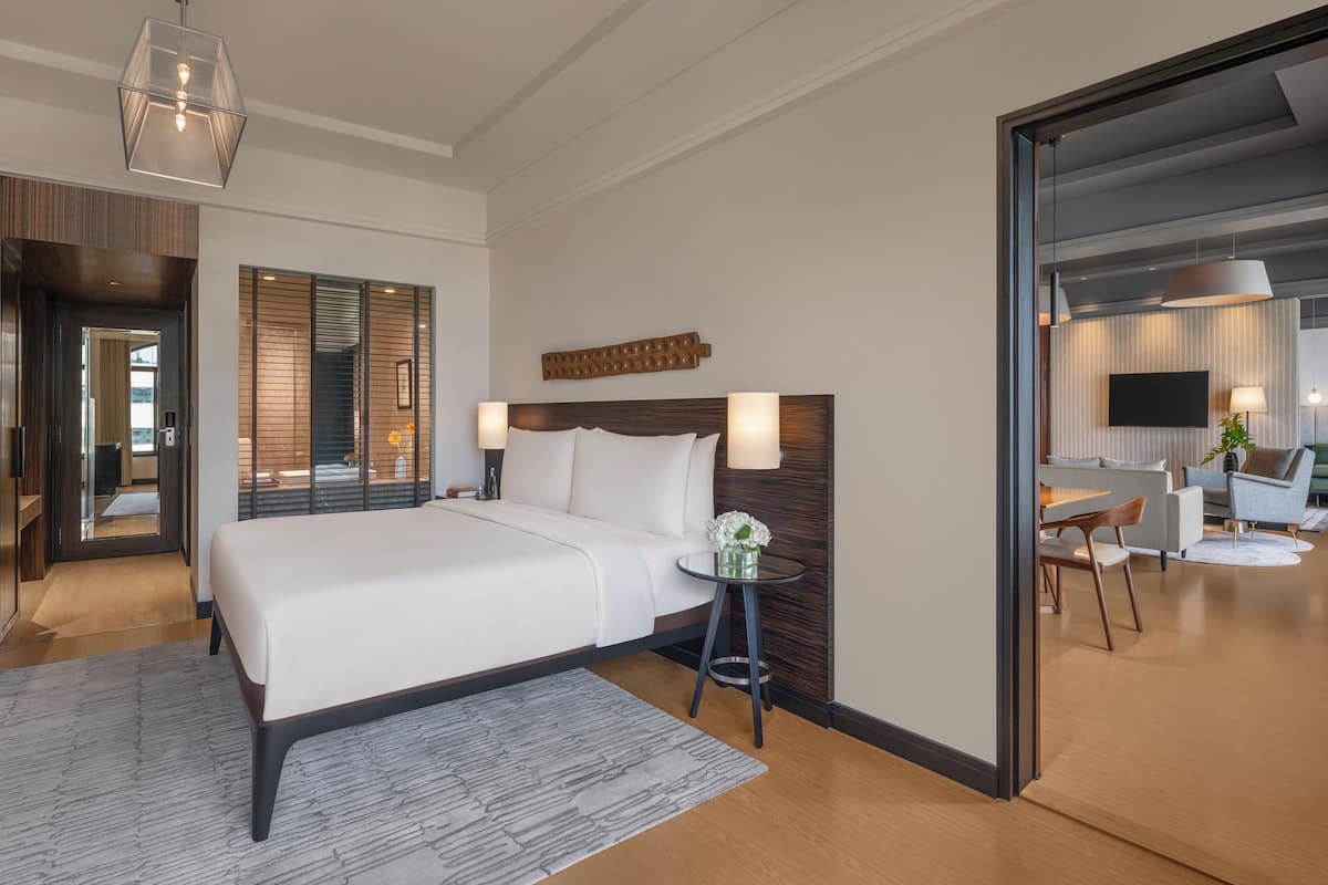 Ein modernes Hotelzimmer mit einem großen Bett, einem kleinen Nachttisch, einem Spiegel und Blick in den Wohnbereich.