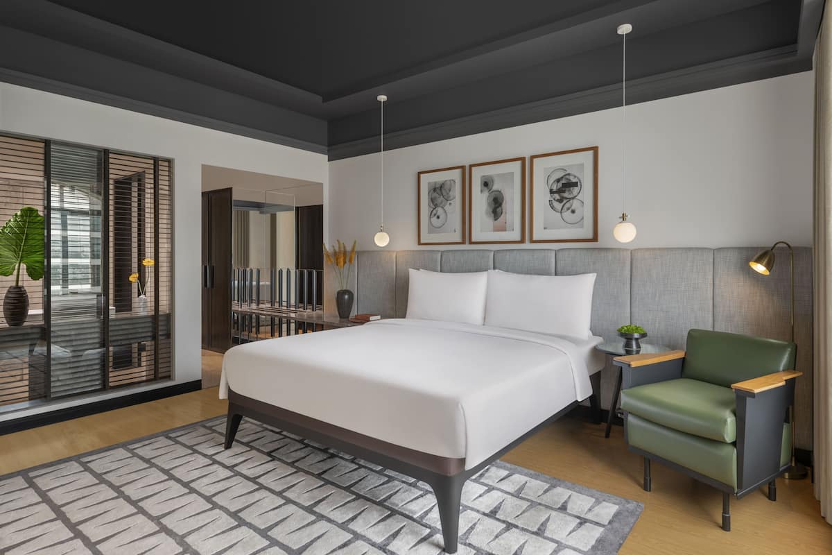 Ein modernes Schlafzimmer mit einem großen Bett, einem grünen Sessel und Kunstwerken an der Wand.