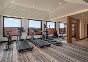 Ein modernes Fitnessstudio mit Laufbändern, Crosstrainern und Gewichtsgeräten. Große Fenster sorgen für natürliches Licht und Blick zum Himmel.