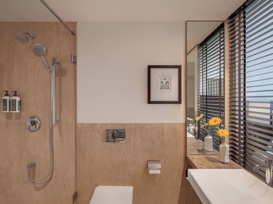 Une salle de bain moderne avec une douche, des toilettes et un lavabo. Un tableau encadré est accroché au mur, et il y a une fenêtre avec des stores.