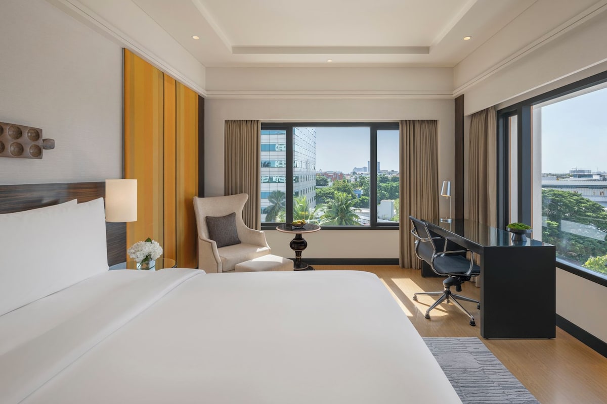 A hotel room with a large bed, a desk, a chair, and a view of the city.