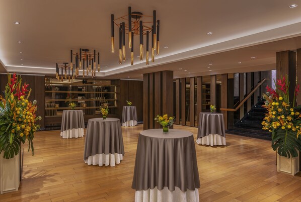 A spacious lobby with round tables, a modern chandelier, and a staircase.