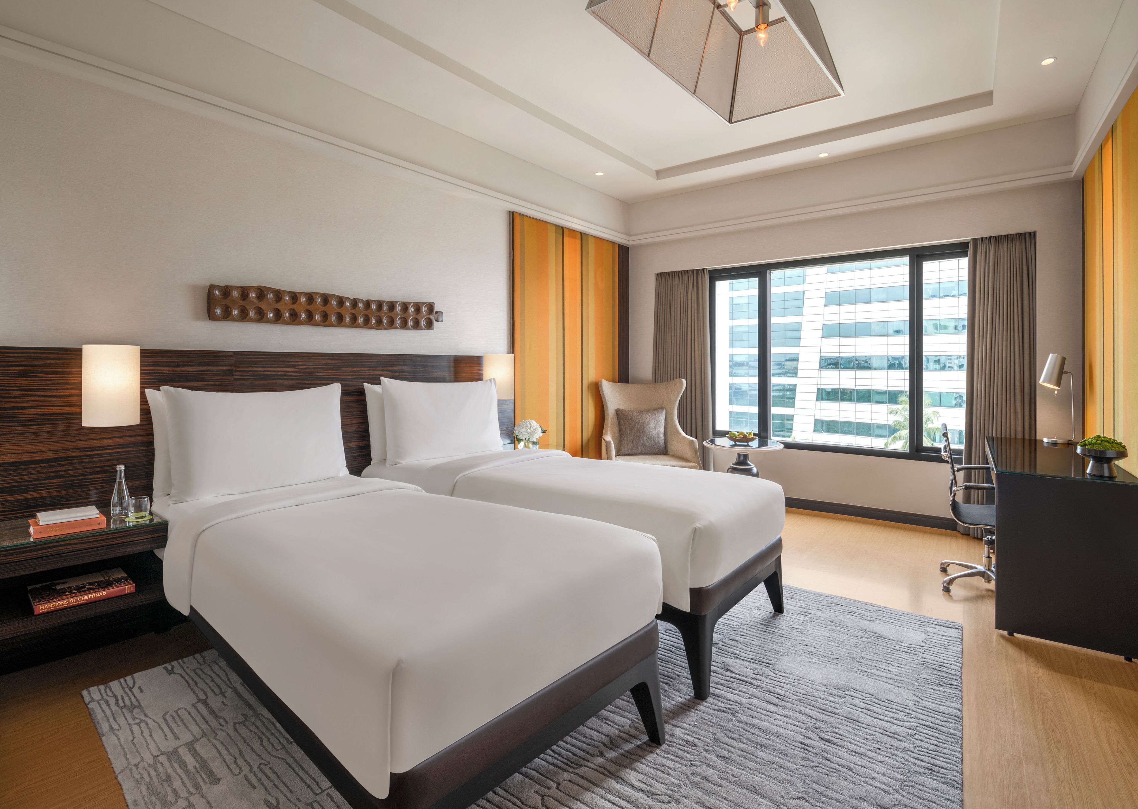 Habitación de hotel con dos camas, un escritorio, una silla y un ventanal con vistas a la ciudad.