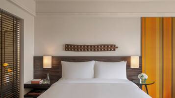 Habitación de hotel con una cama, dos lámparas de noche, una mesita de noche, una pequeña mesa con un jarrón de flores y un panel decorativo en la pared.
