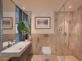 Un baño moderno con un espejo grande, un lavamanos blanco, un inodoro y una ducha.
