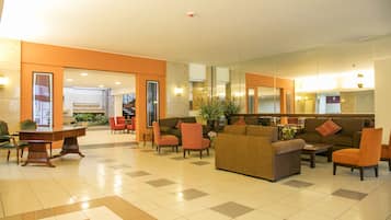 A lobby with a checkered floor, a reception desk, seating area with sofas and chairs, and a large mirror reflecting the space.