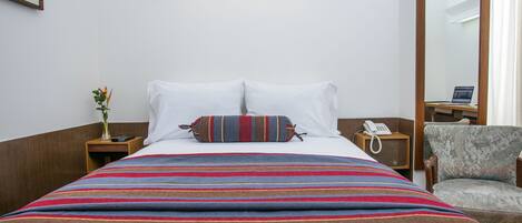 Una habitación de hotel con una cama grande, una mesita de noche con lámpara, una silla y un espejo.