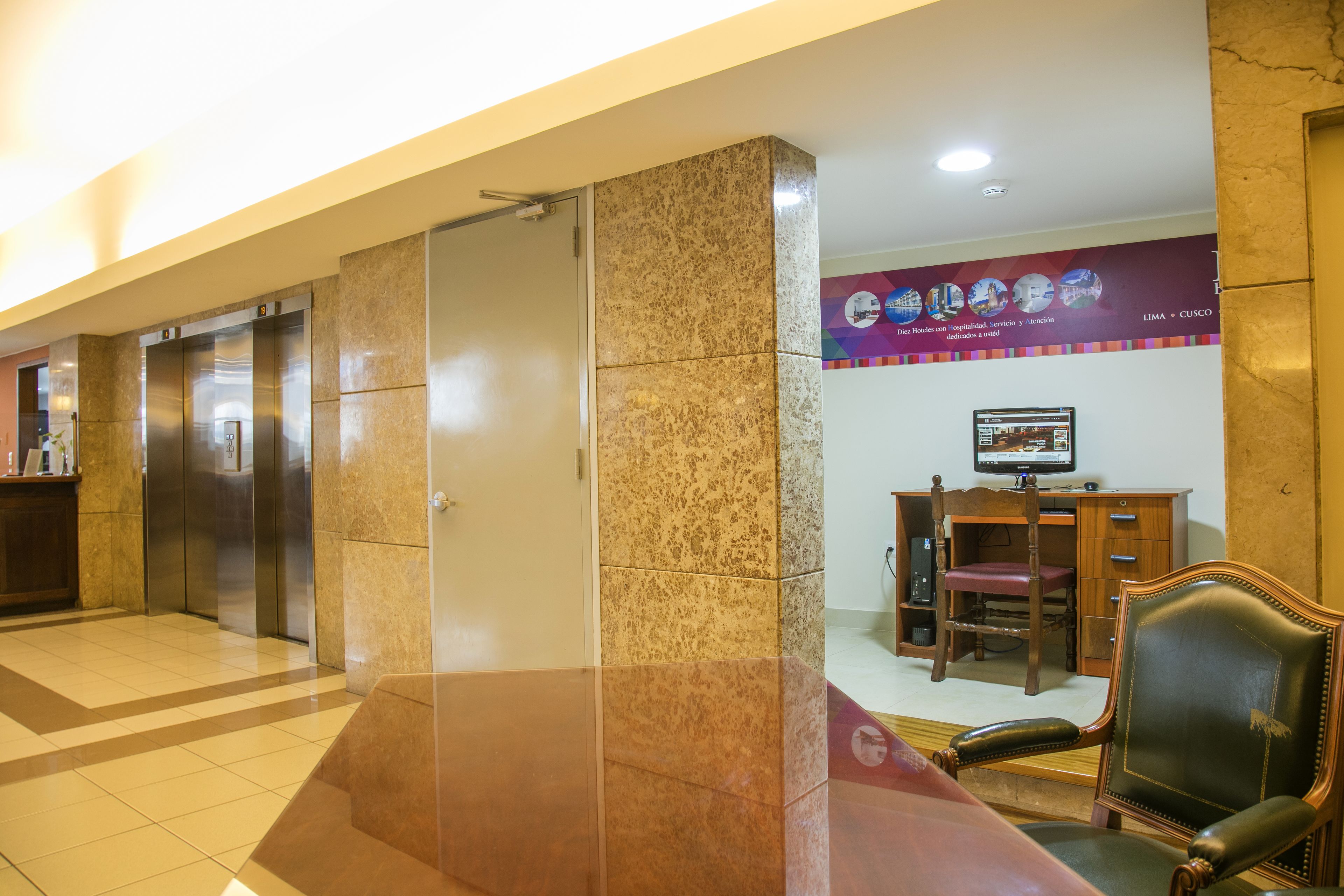 A hotel lobby with elevators, a reception desk, a computer monitor, and a leather chair.