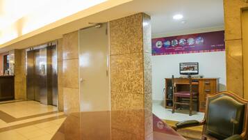 A hotel lobby with elevators, a reception desk, a computer monitor, and a leather chair.