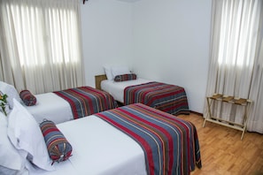 Ein Hotelzimmer mit zwei Einzelbetten, jeweils mit gestreifter Bettdecke und Kissen, einem Holzkopfschild und einem kleinen Holzregal an der Wand.