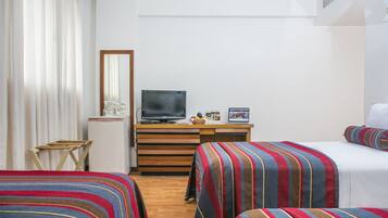 Habitación de hotel con dos camas, televisión, escritorio con computadora y una mesita, y ventana con cortinas.