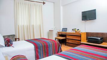 Habitación de hotel con dos camas, un escritorio, televisor y ventana con cortinas.