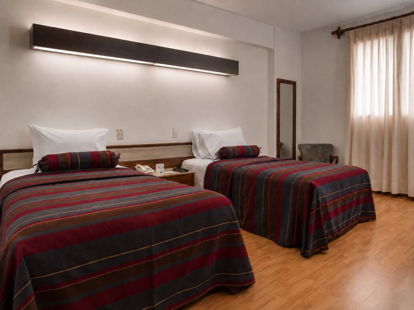 Habitación de hotel con dos camas, una mesita de noche con teléfono, un espejo y una ventana con cortinas.