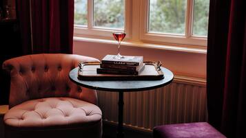 Un sillón con textura, una mesita redonda con una copa de vino tinto y una pila de libros sobre la mesa.