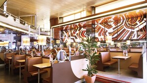 A modern restaurant with booths and tables, a patterned wall, and a potted plant. - Hotel Urpi (Sabadell)