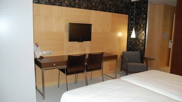 Habitación de hotel con cama, escritorio con dos sillas, televisor y lámpara de pared.