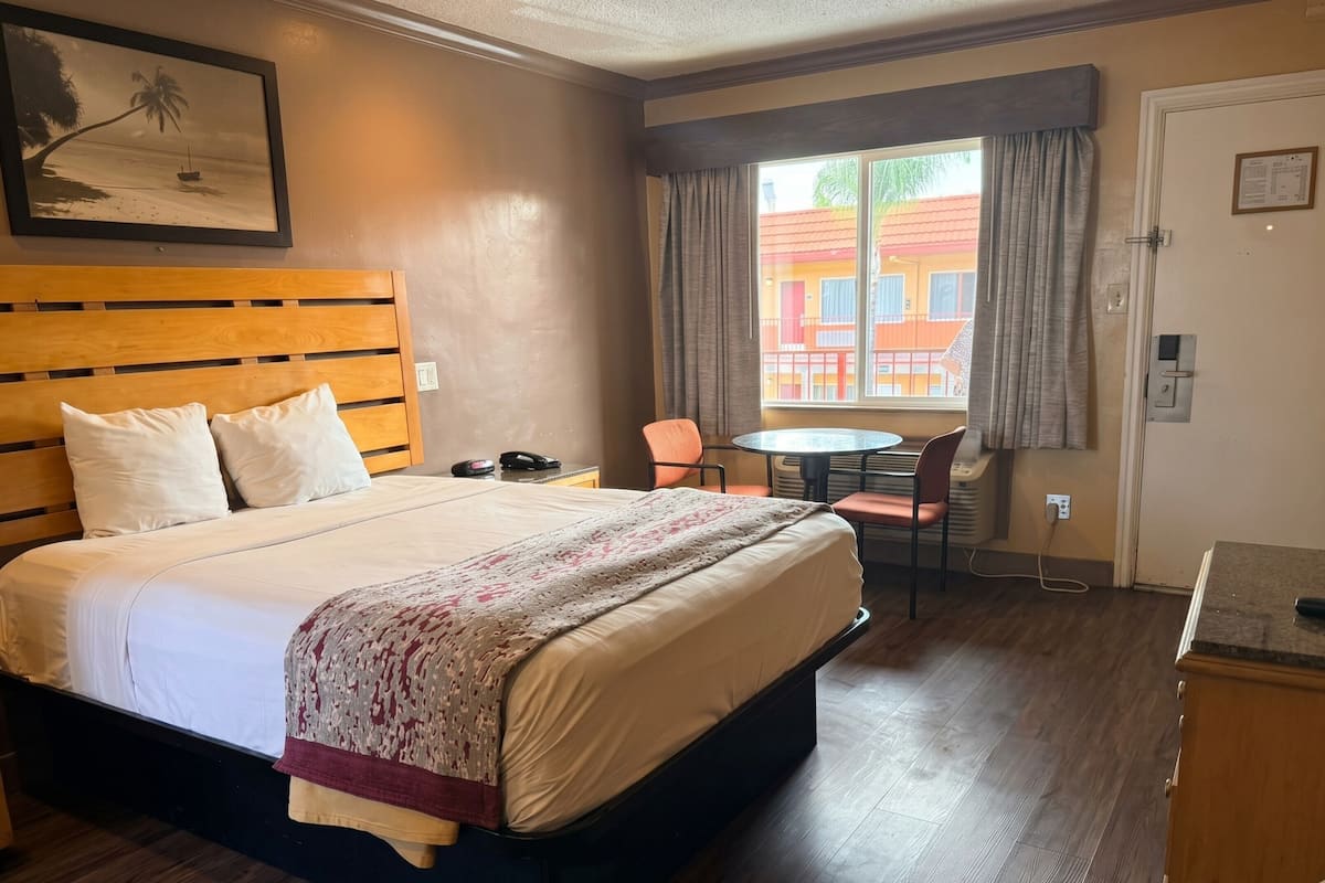 Una camera d'albergo con un letto, una scrivania, una sedia, una finestra con tende e una porta.