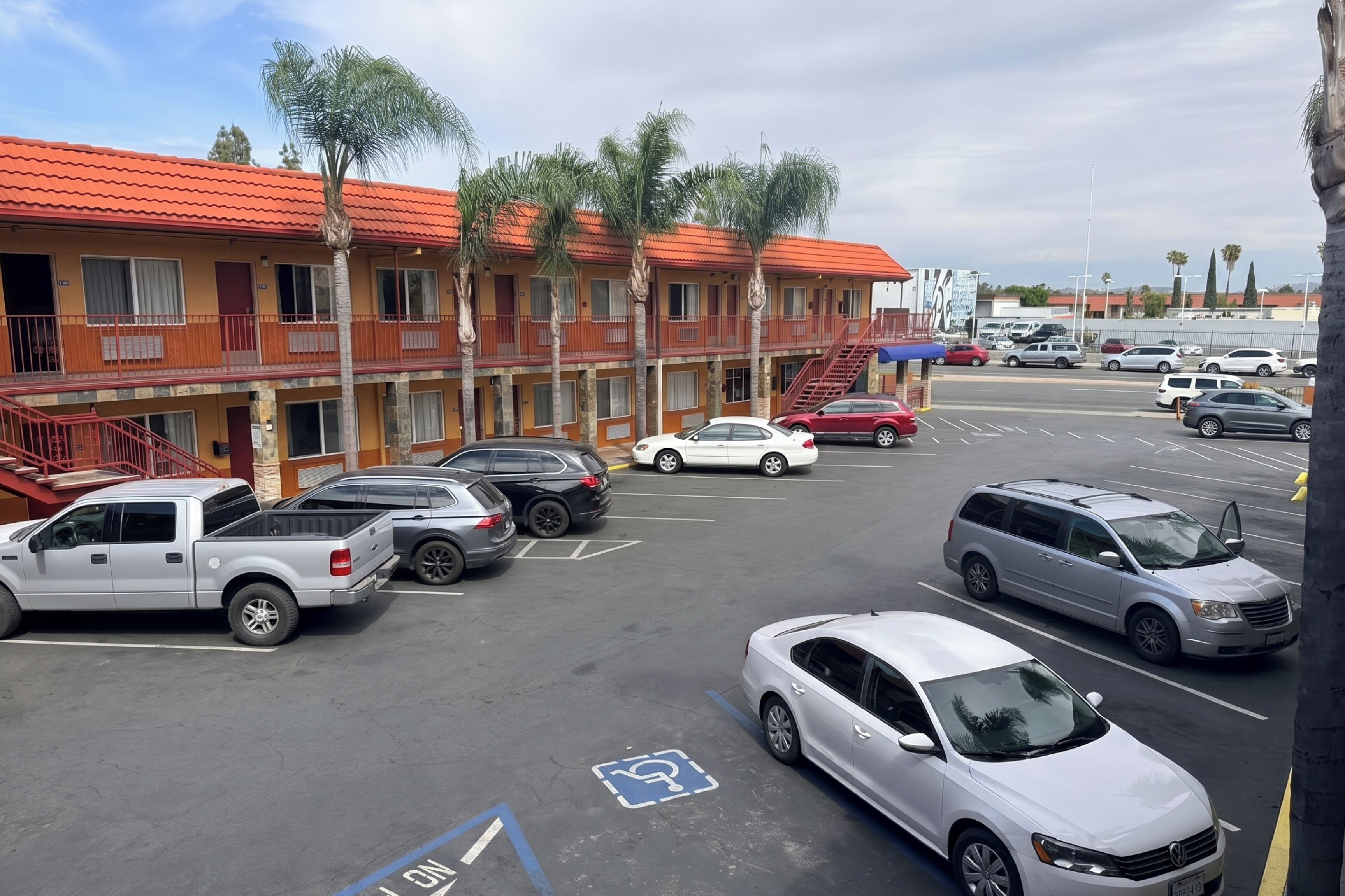 Un estacionamiento con varios autos, un edificio de techo rojo y palmeras.