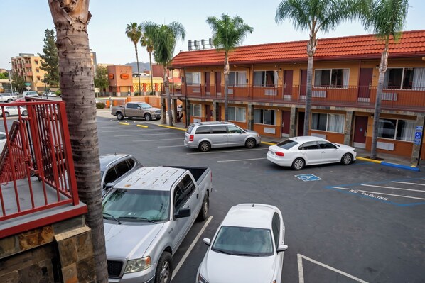 A parking lot with several cars, a red gate, and a building with balconies and palm trees.