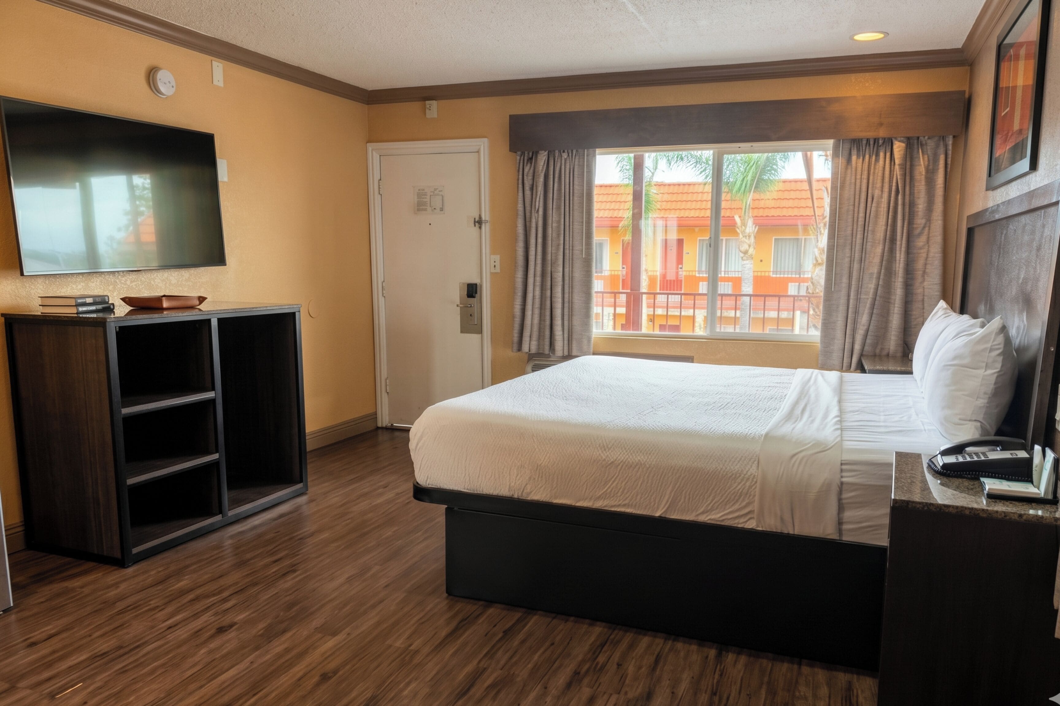 A hotel room with a bed, a TV, a desk, and a window with curtains.