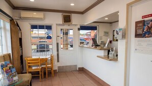 Un espace d’accueil comprenant une table en verre sur laquelle sont disposées des brochures, une chaise en bois, un comptoir d’accueil et une porte donnant sur l’extérieur.