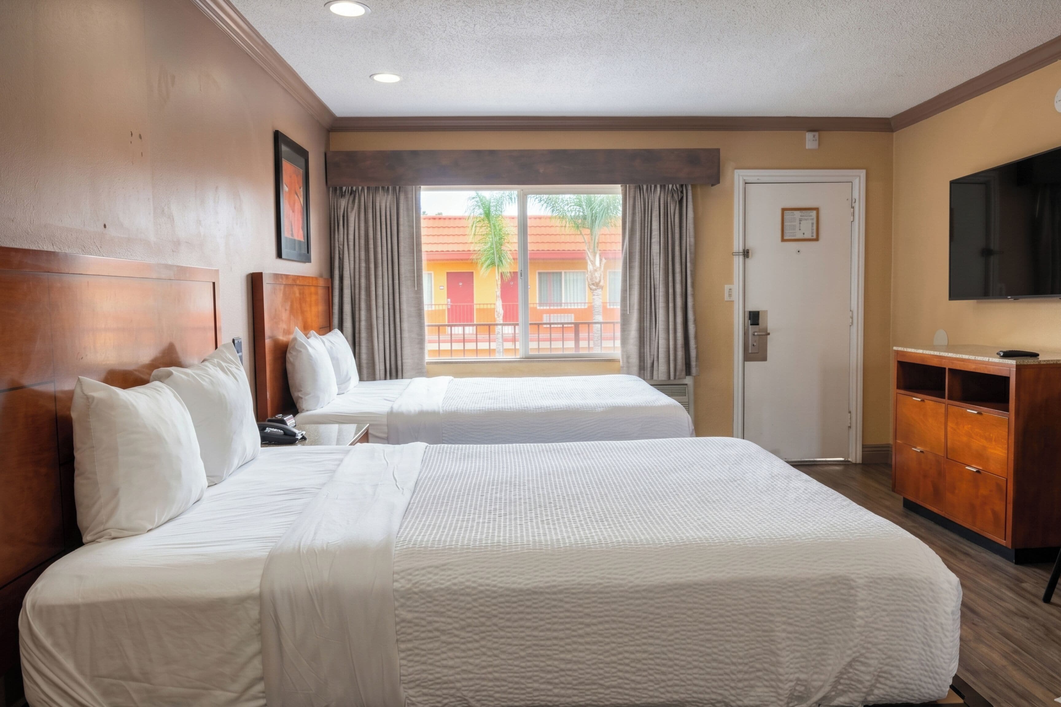 A hotel room with two beds, a TV, a wardrobe, and a window with a view of buildings.