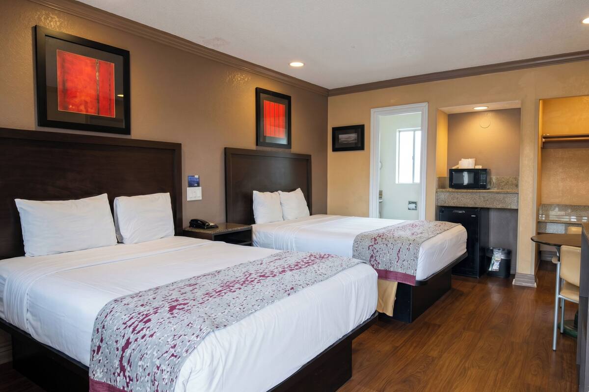 Una camera d'albergo con due letti, un forno a microonde, un angolo cottura e una porta che dà su un'altra stanza.