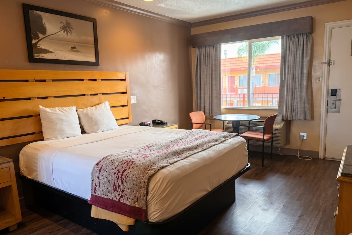 Una camera d'albergo con un letto grande, una scrivania, una sedia, una finestra con tende e un quadro appeso al muro.