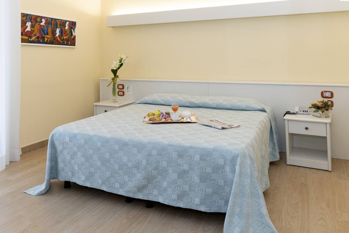 A neatly arranged bedroom with a bed, bedside tables, and a painting on the wall.