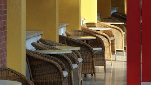 A row of wicker chairs and tables in a sunlit corridor with yellow walls and red accents.
